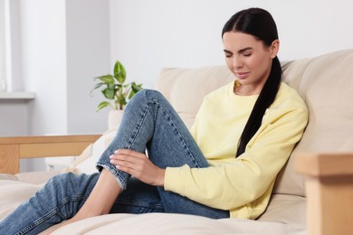 Photo of Woman suffering from leg pain on sofa at home