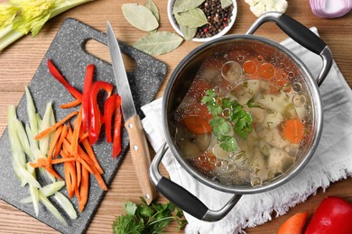 Pot of delicious vegetable bouillon and ingredients on wooden table, flat lay