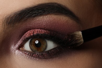 Applying dark eye shadow with brush onto woman's face, closeup. Beautiful evening makeup