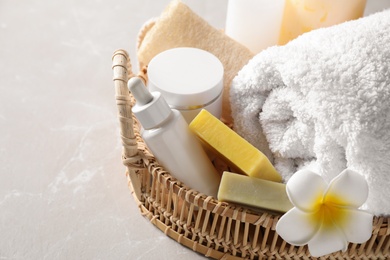 Wicker tray with fresh towel, plumeria flower and toiletries on light table, closeup. Spa treatment