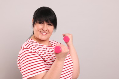Happy overweight mature woman doing exercise with dumbbells on grey background. Space for text