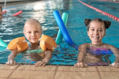 Little girls with swimming noodles in indoor pool