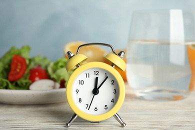 Alarm clock and healthy food on white wooden table. Meal timing concept