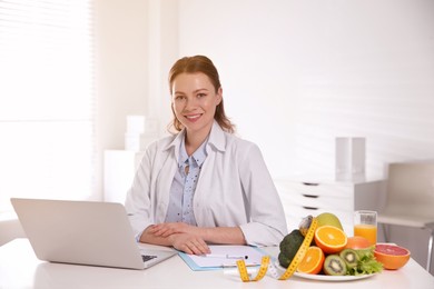 Nutritionist with clipboard and laptop at desk in office