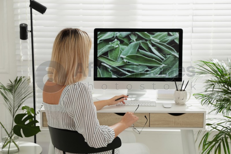 Photo of Woman working on computer at table in room, back view. Interior design