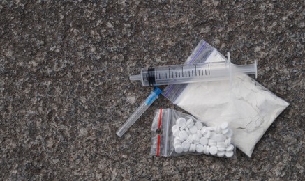 Photo of Plastic bag with powder, syringe, pills on stone surface, flat lay and space for text. Hard drugs