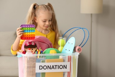 Cute little girl putting toy into donation box at home, space for text