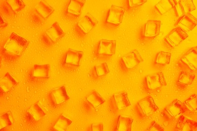 Cold ice and water drops on orange background, flat lay. Ingredient for refreshing drink