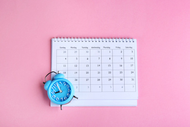 Calendar and alarm clock on pink background, flat lay