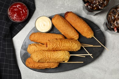 Delicious deep fried corn dogs with board and sauces on light grey table, flat lay