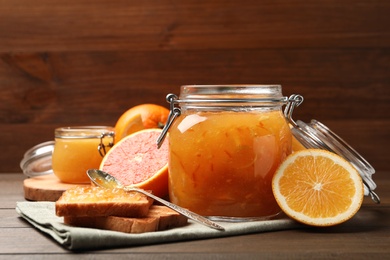 Delicious orange marmalade, fresh fruits and toasts on wooden table