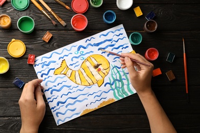 Girl painting picture of fish on table, top view