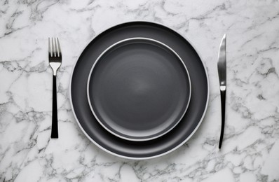New dark plates and cutlery on white marble table, flat lay