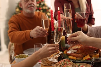 Family clinking glasses of drinks at festive dinner, focus on hands. Christmas celebration
