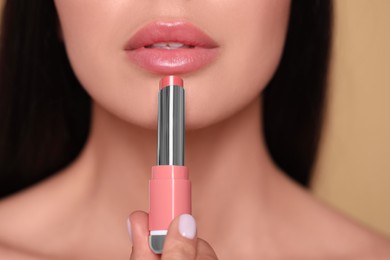 Photo of Young woman applying nude lipstick on beige background, closeup