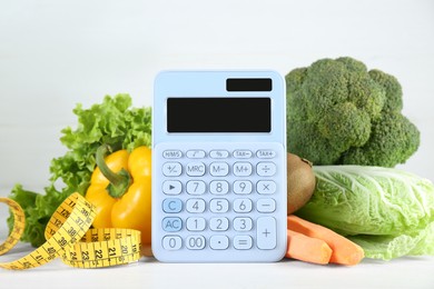 Calculator and food products on white wooden table. Weight loss concept