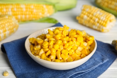 Tasty sweet corn kernels in bowl and fresh cobs on table