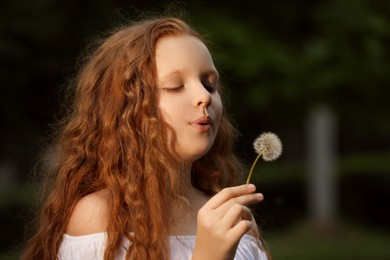 Girl with red hair blowing dandelion in park