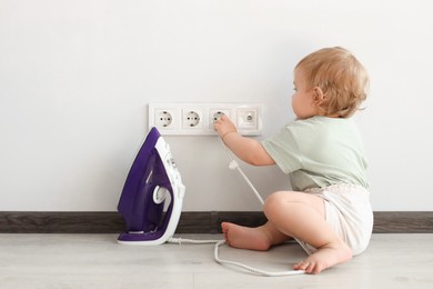 Cute baby playing with electrical socket and iron plug at home. Dangerous situation