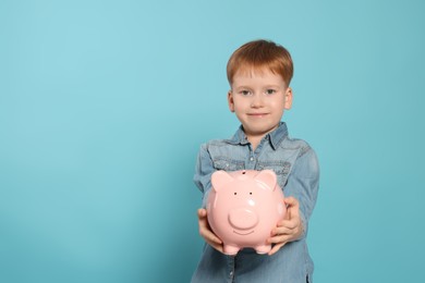 Cute little boy with ceramic piggy bank on light blue background, space for text