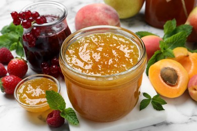 Jars with different jams and fresh fruits on white marble table, closeup