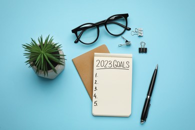Photo of Making goals for 2023 new year. Flat lay composition with notebook on light blue background