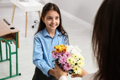 Schoolgirl congratulating her pedagogue with bouquet in classroom. Teacher's day