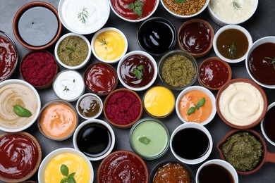 Photo of Many different sauces and herbs on black table, flat lay