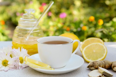Photo of Cup of delicious tea with honey, lemon and ginger on white table outdoors