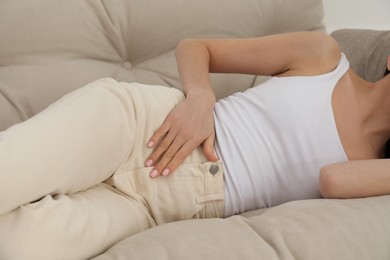 Woman suffering from appendicitis inflammation on sofa indoors, closeup