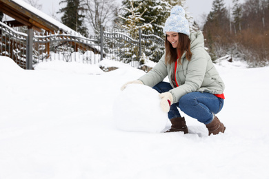 Happy woman making ball for snowman outdoors. Winter vacation
