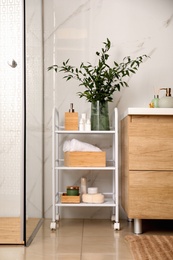 Vase with green branches and different toiletries on rack in bathroom