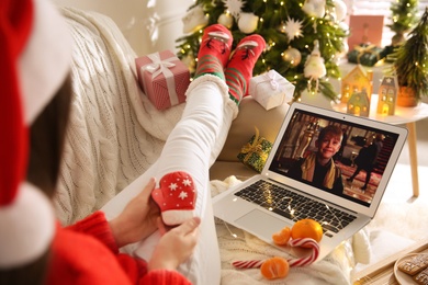 MYKOLAIV, UKRAINE - DECEMBER 25, 2020: Woman with gingerbread watching Home Alone movie on laptop indoors, closeup. Cozy winter holidays atmosphere