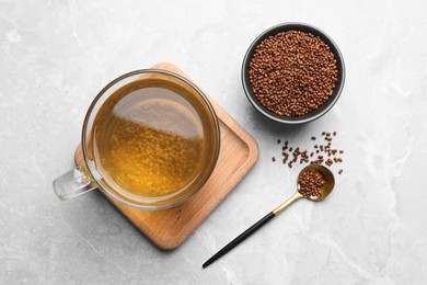 Cup of aromatic buckwheat tea and granules on light marble table, flat lay