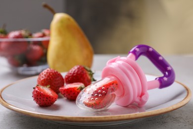 Plastic nibbler with fresh strawberries on light table, closeup. Baby feeder