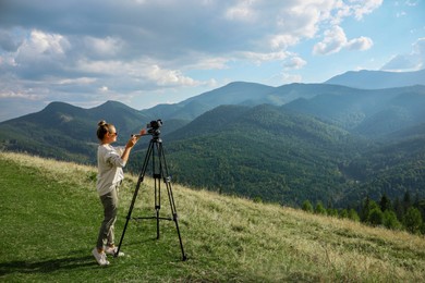 Professional photographer with modern camera on tripod in mountains. Space for text