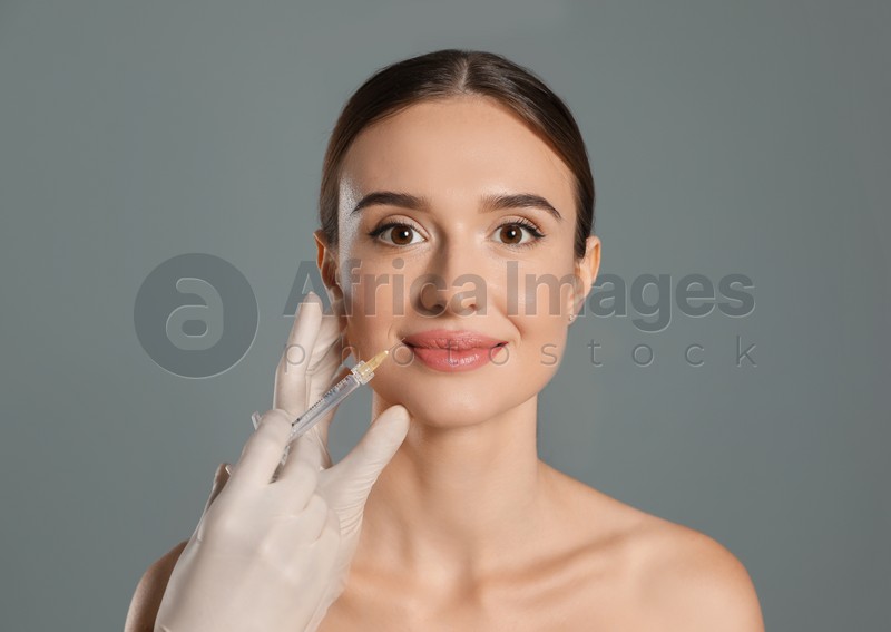Beautiful woman getting facial injection on grey background. Cosmetic surgery