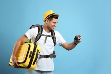 Male tourist with travel backpack, suitcase and camera on turquoise background