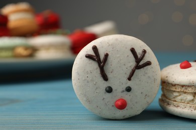 Tasty reindeer Christmas macarons on light blue wooden table against blurred festive lights, closeup