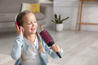 Cute little girl in headphones with hairbrush singing at home