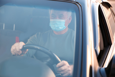 Senior man with medical mask in car. Virus protection