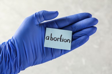 Doctor holding paper card with word ABORTION on light background, closeup