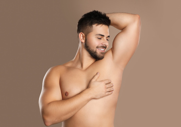 Young man showing hairless armpit after epilation procedure on brown background