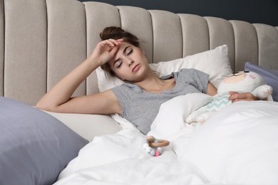 Exhausted young mother with toy sleeping in bed at home