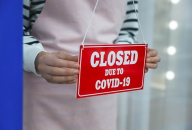Business owner hanging red sign with text Closed Due To Covid-19 onto glass door, closeup. Coronavirus quarantine