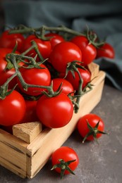 Many ripe red tomatoes in wooden crate on grey table, closeup