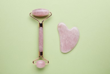 Photo of Rose quartz gua sha tool and facial roller on light green background, flat lay