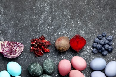 Photo of Painted Easter eggs with natural organic dyes (blueberries, beetroot, hibiscus, and red cabbage) on black table, flat lay. Space for text