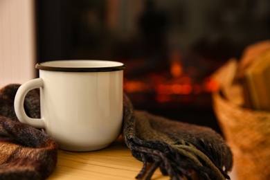 Mug with hot drink and plaid against fireplace, space for text