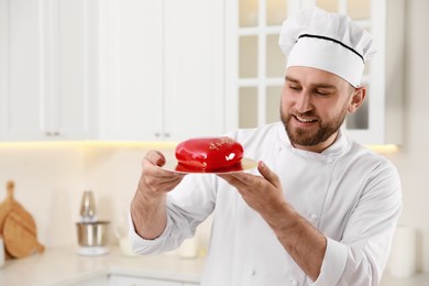 Happy professional confectioner holding delicious cake in kitchen